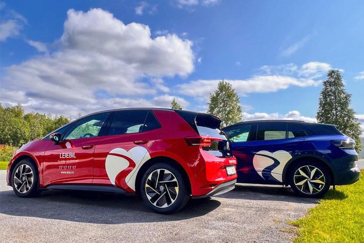 To biler med fargerike design, en rød og en blå, parkert på en vei med trær og blå himmel i bakgrunnen.
