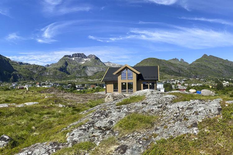 Moderne hytte med store vinduer, omgitt av fjell og grønt landskap i Norge.