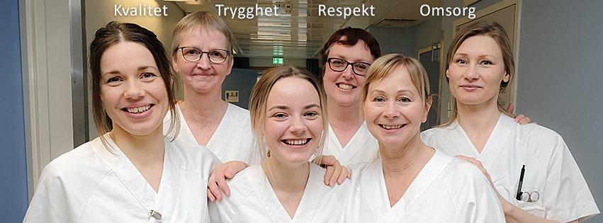 Seks smilende helsearbeidere i hvite uniformer står sammen i en sykehusgang.