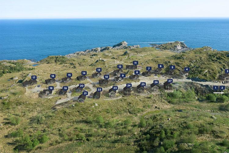 Utsikt over kystlandskap med flere hytter nummerert langs bakken nær havet.