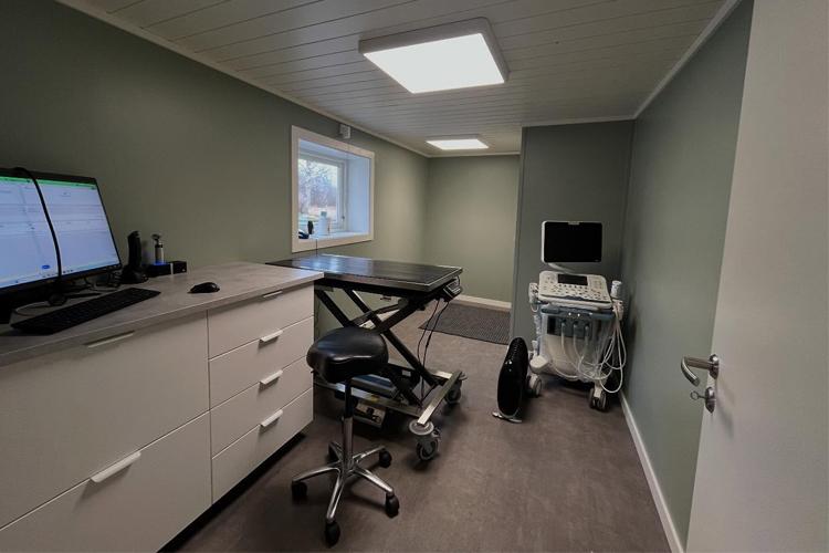 Moderne kontor med skrivebord, datamaskiner og medisinsk utstyr i et lyst rom med grønne vegger.