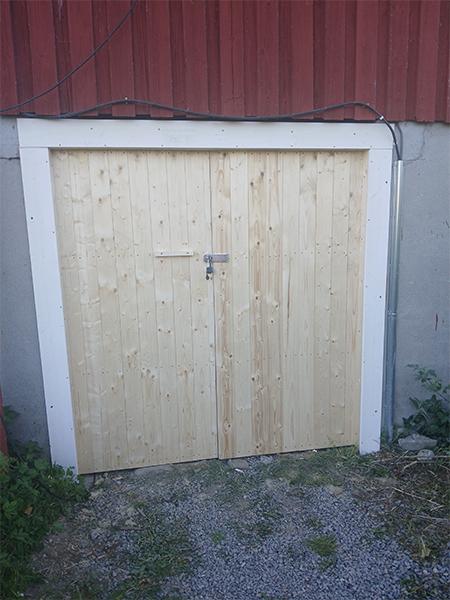 En ny treport med lås, plassert på en grå steinlagt bakgård ved en rød bygning.