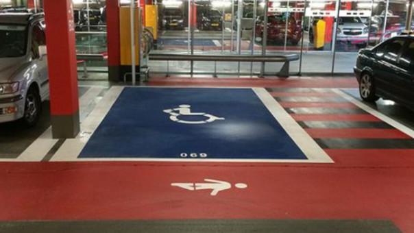 Handikapparkering med blått symbol og rød bakgrunn i parkeringshus.