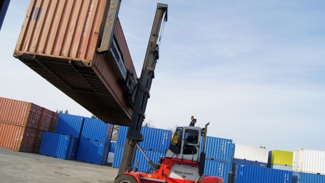 Gaffeltruck løfter en fraktcontainer på en lagerplass med flere containere i bakgrunnen.