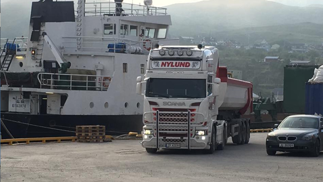 En lastebil fra Nylund kjører ved havnen, med en båt og containere i bakgrunnen.