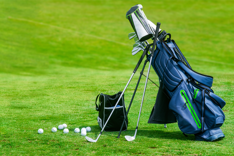 En golfbag med klubber står på gresset, med golfballer spredt rundt.