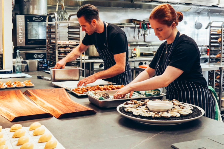 Kokker som forbereder mat på en restaurantkjøkken med ulike retter på bordet.
