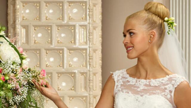 Brud i hvit brudekjole smiler mens hun holder en blomsterbukett i en elegant setting.