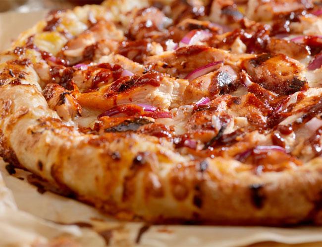 En nærbilde av en pizza med kylling, rødløk og BBQ-saus på en sprø bunn.