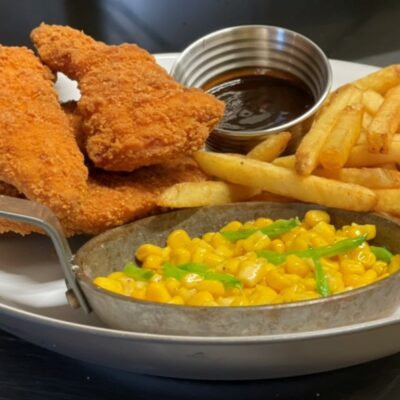 Sprø kyllingfileter med pommes frites og mais med grønne paprika i en metallskål, servert med BBQ-saus.