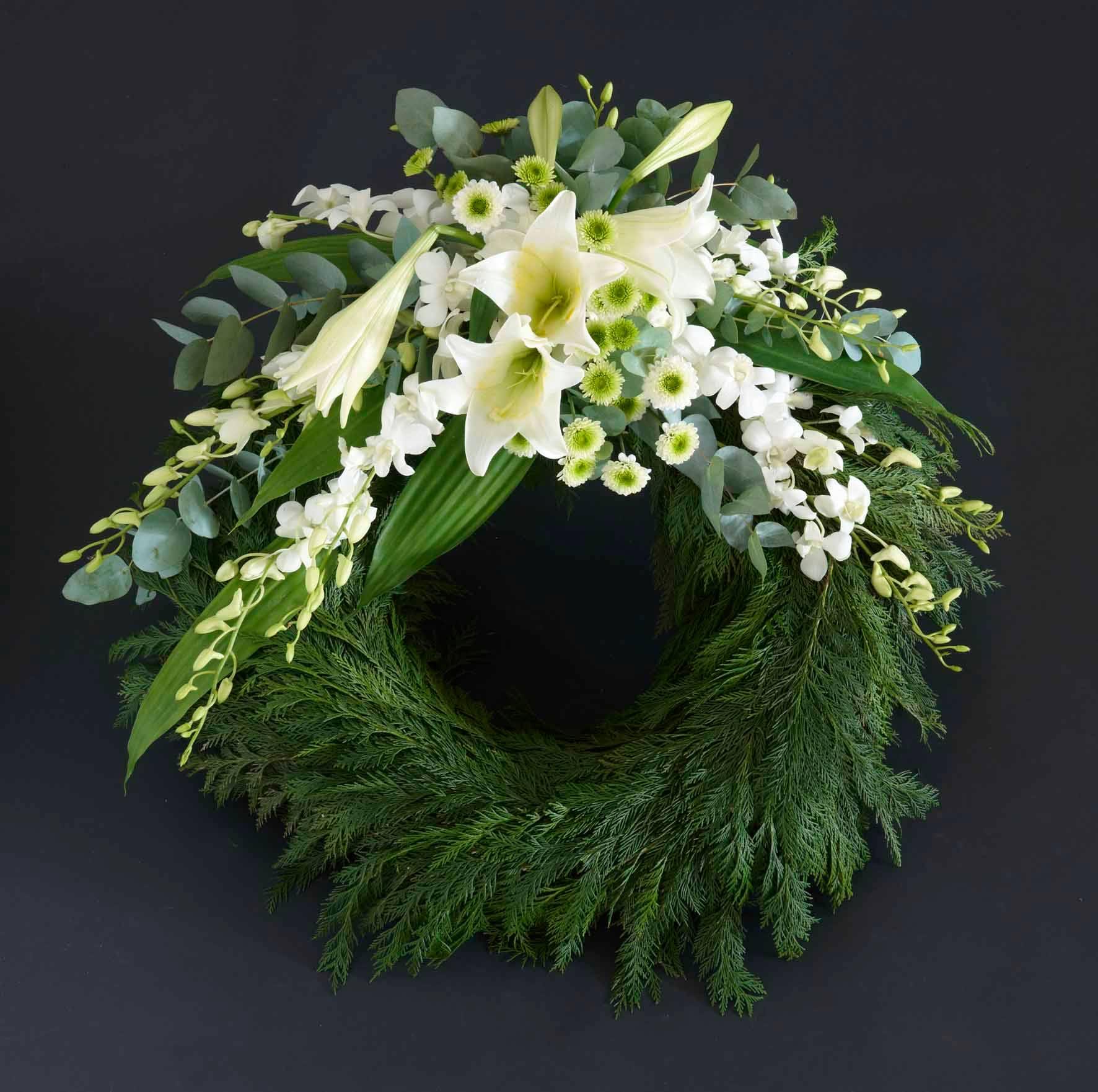 En vakker krans laget av hvite blomster og grønt, inkludert liljer og eukalyptus, på en mørk bakgrunn.