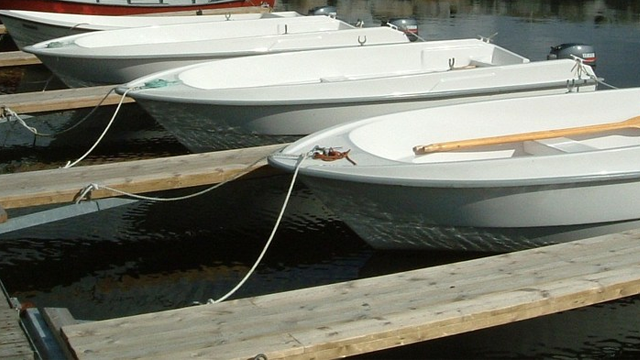 Flere hvite båter fortøyd til en brygge ved vannet, med motorer synlige bak.