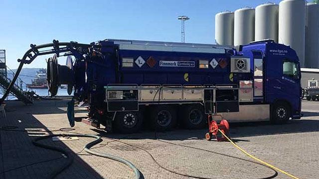 En blå tankbil med slanger og utstyr står parkert ved havnen, klar for oppdrag.