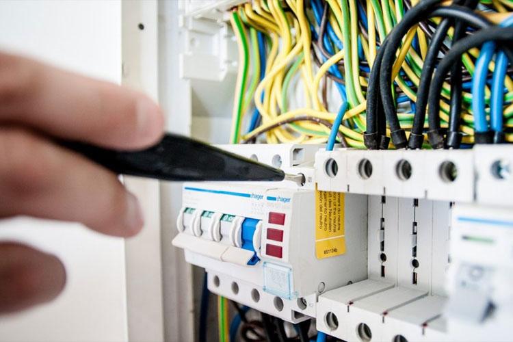En hånd som bruker en skrutrekker på en elektrisk tavle med fargerike ledninger.