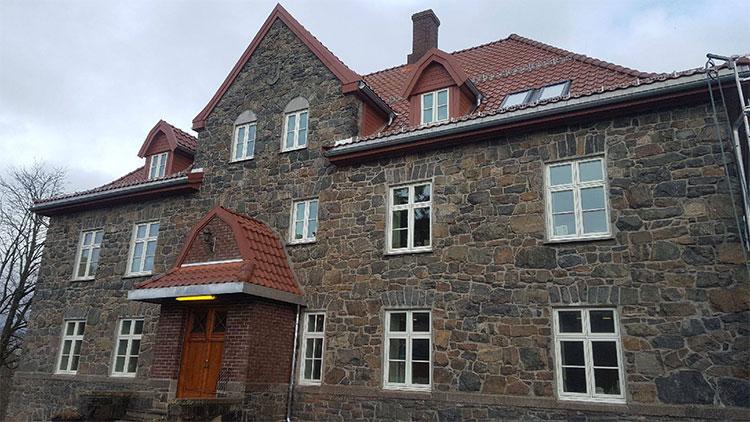 En stor steinbygning med rødt tak og mange vinduer, beliggende under en grå himmel.
