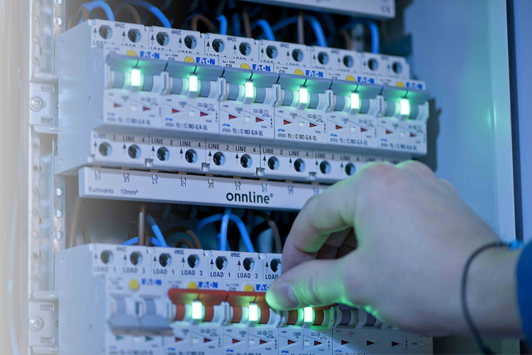 En hånd justerer lysene på en elektrisk tavle med flere brytere og ledninger.