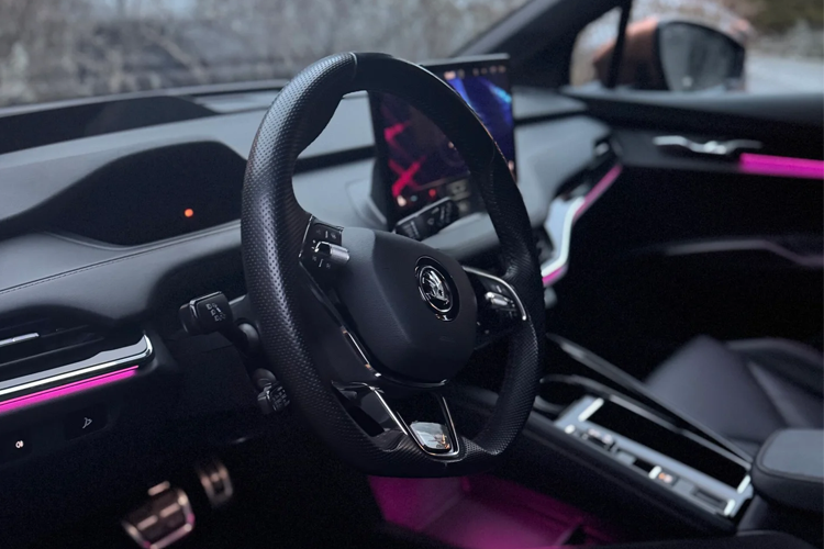 Interiør av en moderne bil med et sportslig ratt og en stor skjerm, belyst med rosa LED-lys.