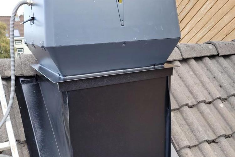Grå ventilasjonshette plassert på taket, med takstein i bakgrunnen.