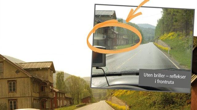 Bilde av en vei med bygninger langs siden, med refleksjoner i frontruten på en bil.