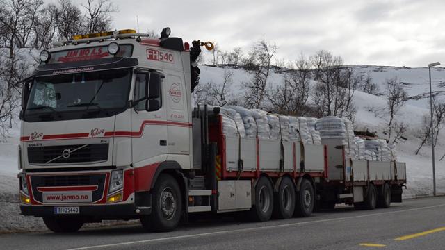 En stor lastebil med tilhenger som frakter pakker på en vei i snødekt landskap.