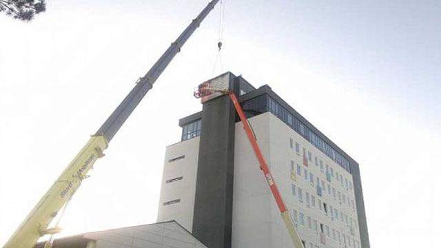 Bygning med kran og lift som arbeider på taket under klar himmel.