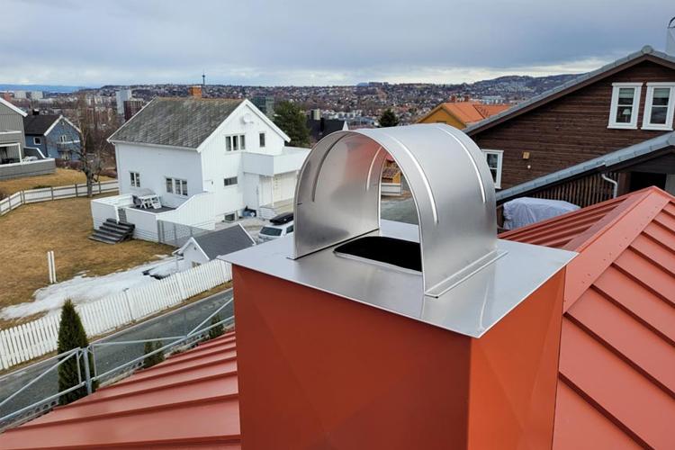 Kaminhette i rustfritt stål på taket av et hus med utsikt over nabolaget og landskapet.