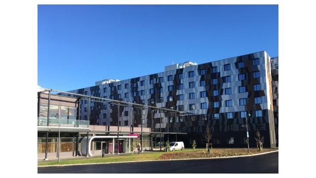 Moderne hotellbygning med glassfasade og flere etasjer under klar blå himmel.