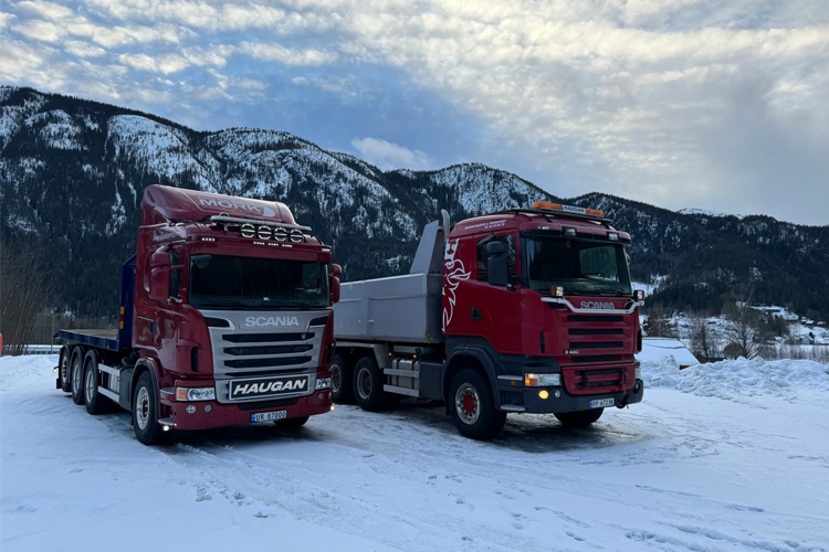 To lastebiler fra Scania parkert i snøen med fjell i bakgrunnen.