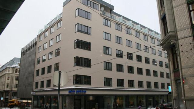 Moderne kontorbygg med mange vinduer og en lys fasade i en bygate. Snø på bakken og grå himmel.