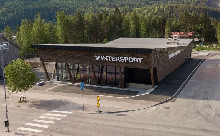 Moderne Intersport-butikk med trepanel og store vinduer, omgitt av grønt landskap og veier.