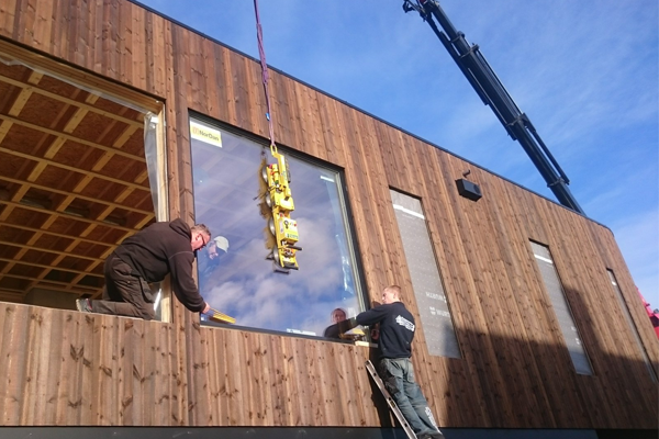 To install store vinduer på en moderne trebygning med håndverkere og kran.