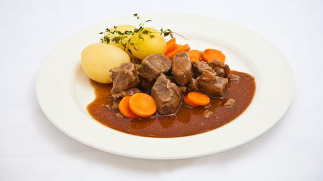 En tallerken med kjøttgryte, poteter, gulrøtter og urter, servert med en rik brun saus.