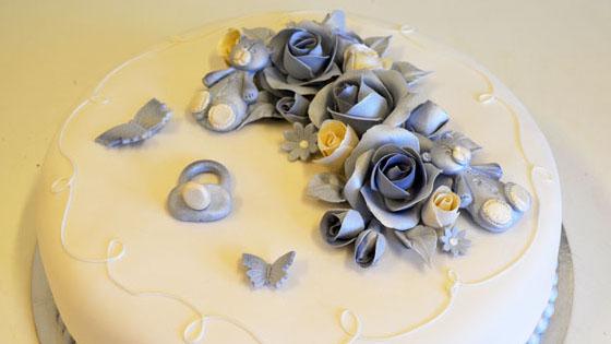 En vakker kake dekorert med blå og hvite roser, sommerfugler og et hjerte i fondant.