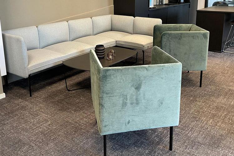Moderne stue med en lys sofa og to grønne stoler rundt et svart bord.
