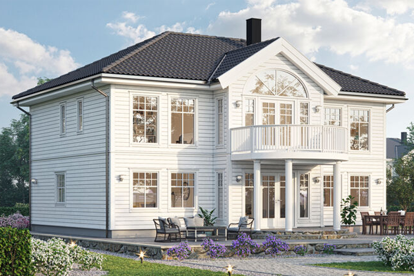 Moderne, hvitt hus med balkong og store vinduer, omgitt av blomster og grøntområde.