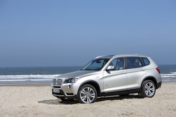 En sølvfarget BMW SUV parkert på en strand med havet i bakgrunnen.