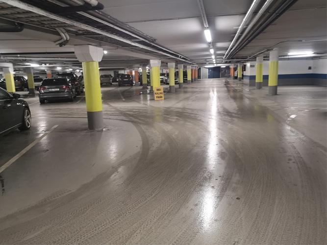 Tomt parkeringshus med biler, gule søyler og glatte gulvflater. Belysningen er sterk og jevn.