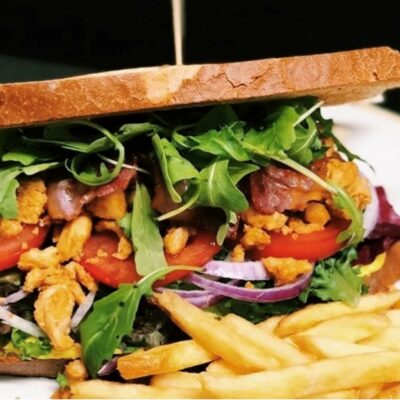 En saftig sandwich med kylling, tomater, rødløk, salat og pommes frites på siden.