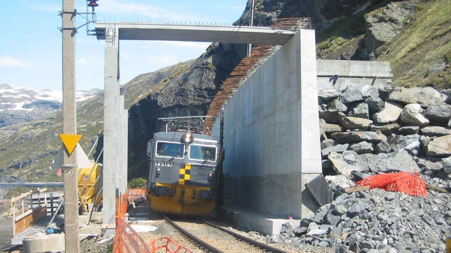 Tog som kjører gjennom en tunnel med stein og bygninger i fjellandskap.