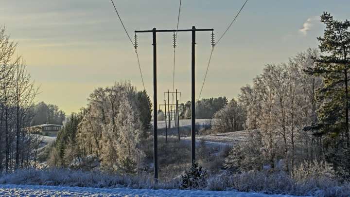 En vinterlig landskap med høyspentlinjer, snødekte trær og frost på bakken.