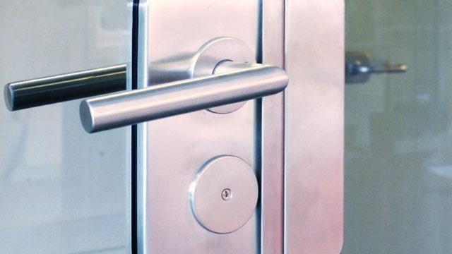 Nærbilde av en moderne dørhåndtak og lås i rustfritt stål på en glassdør.
