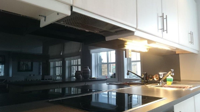 Moderne kjøkken med svart benkeplate, komfyr og overskap, belyst av taklampe og vinduer i bakgrunnen.