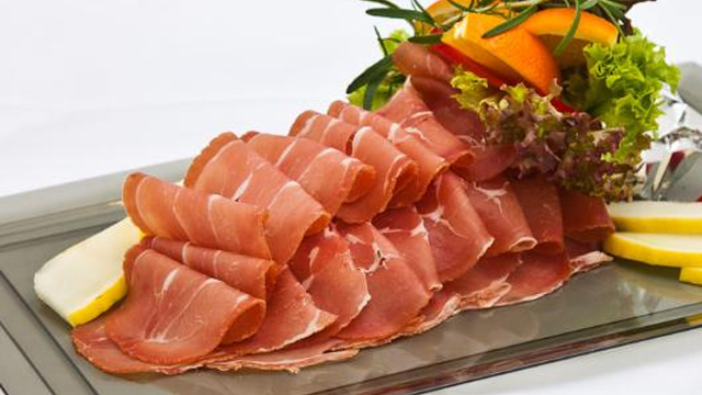 Skiver av spekeskinke servert på et fat med salat og sitronbiter.