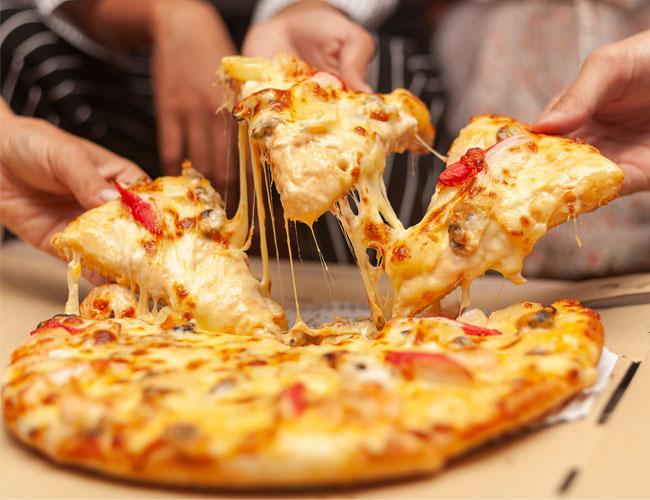 En nybakt pizza med smeltet ost og grønnsaker, delt opp av flere hender.