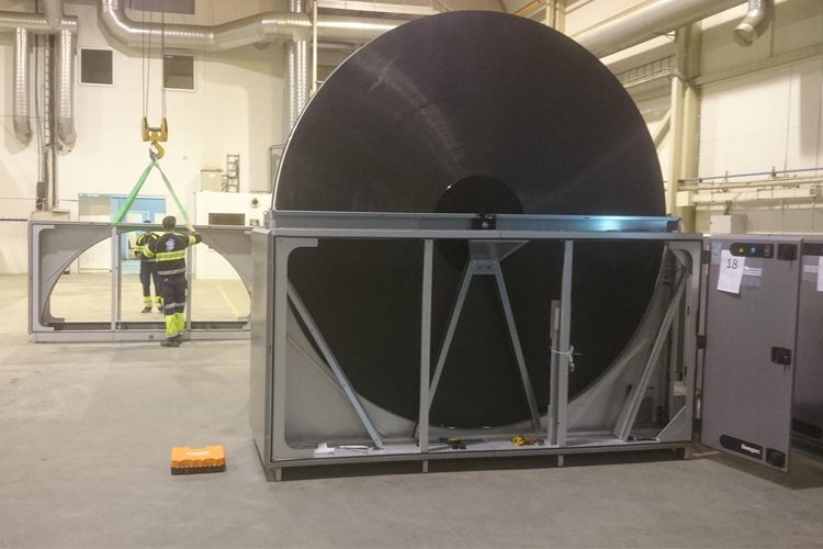 En stor svart rull med metallramme i en fabrikk, med en arbeider som heiser en del av utstyret.