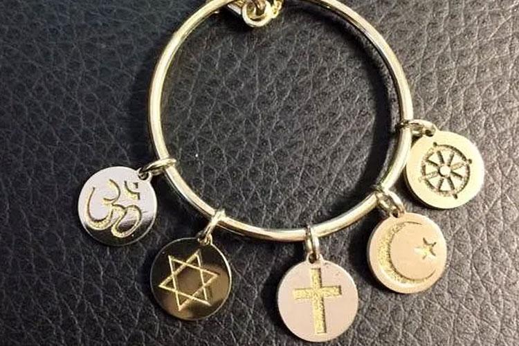 Et gullbelagt armbånd med fem symboler fra ulike religioner, inkludert Om, Davidstjernen, et kors, månen og dharmasirkelen.