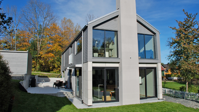 Moderne hus med store vinduer, beliggende i en hage med trær i høstfarger.