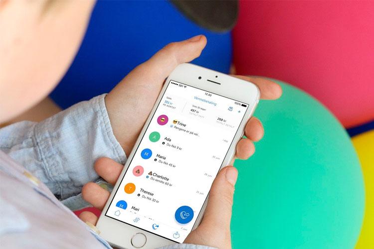 En person holder en smarttelefon med en app åpen, omgitt av fargerike baller.