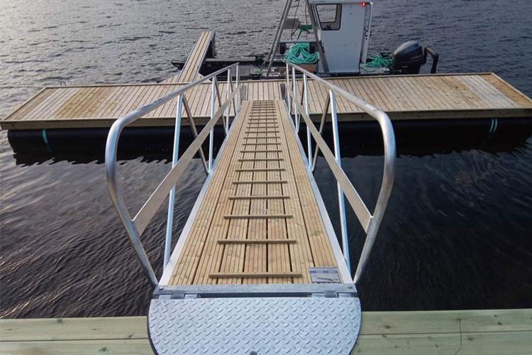 Bilde av en brygge med en rampe som fører til en plattform på vannet, omringet av rolig vann.