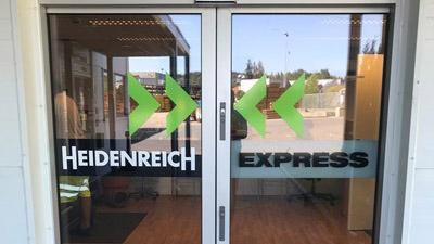 Inngangsdører til Heidenreich Express med grønne piler og logo i vinduet.